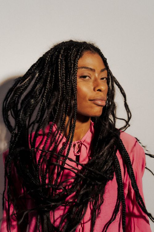 Free Stylish portrait of a woman in a pink shirt with long braided hair posing confidently against a neutral background. Stock Photo