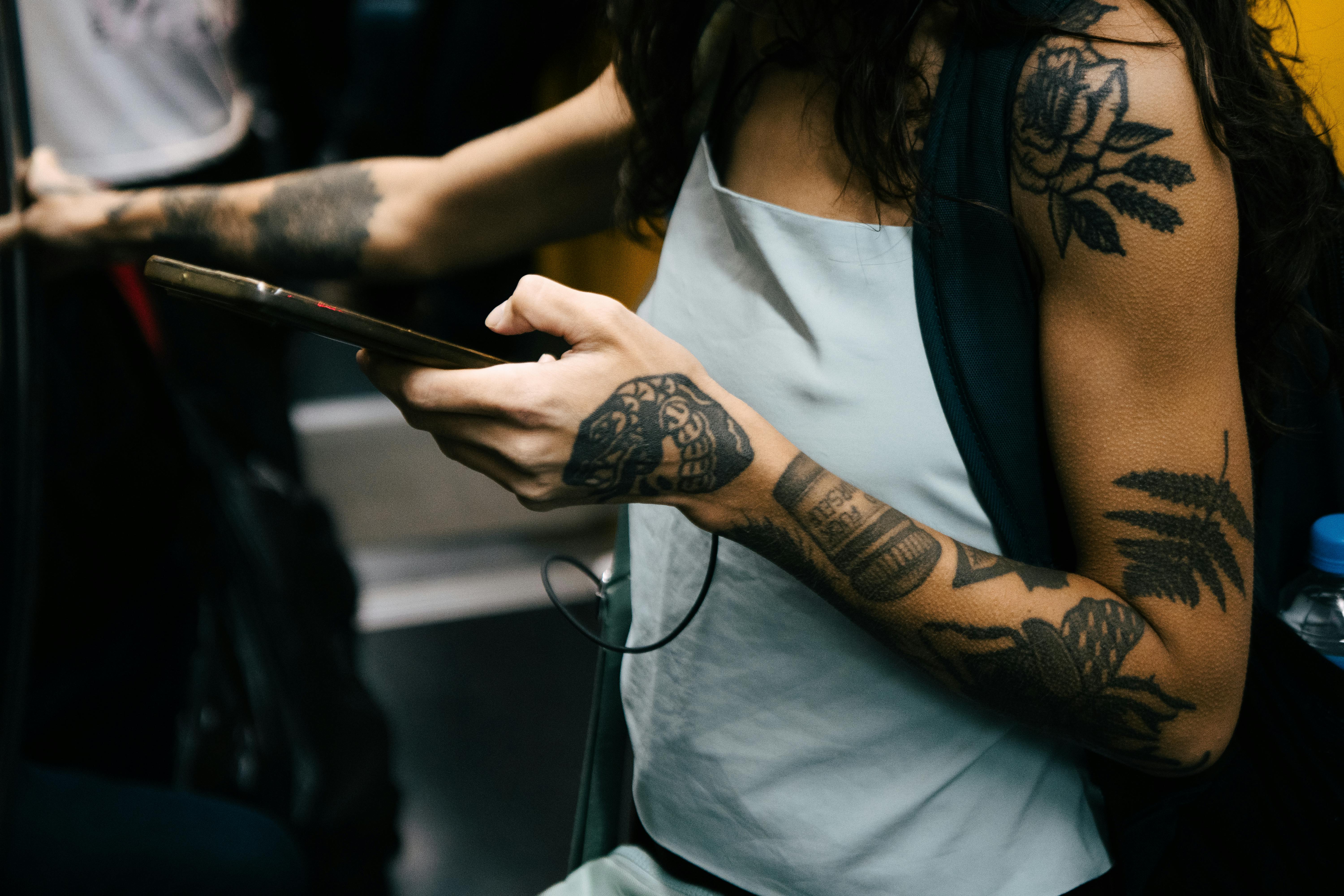 Gratis En person med tatoveringer bruker en smarttelefon på offentlig transport, og viser frem en moderne livsstil. Arkivbilde