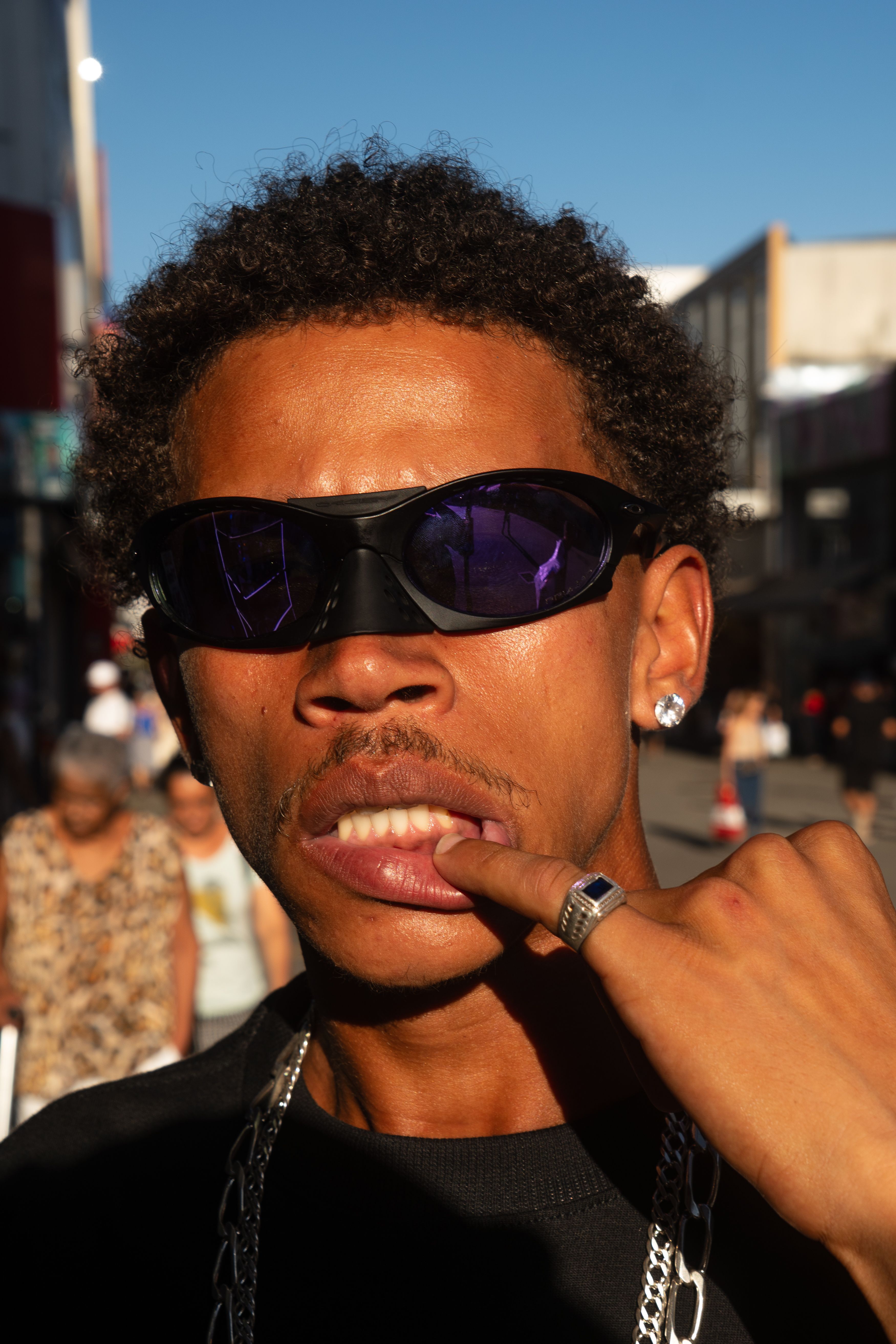 Close-up of a stylish man wearing sunglasses posing confidently on a sunny urban street.