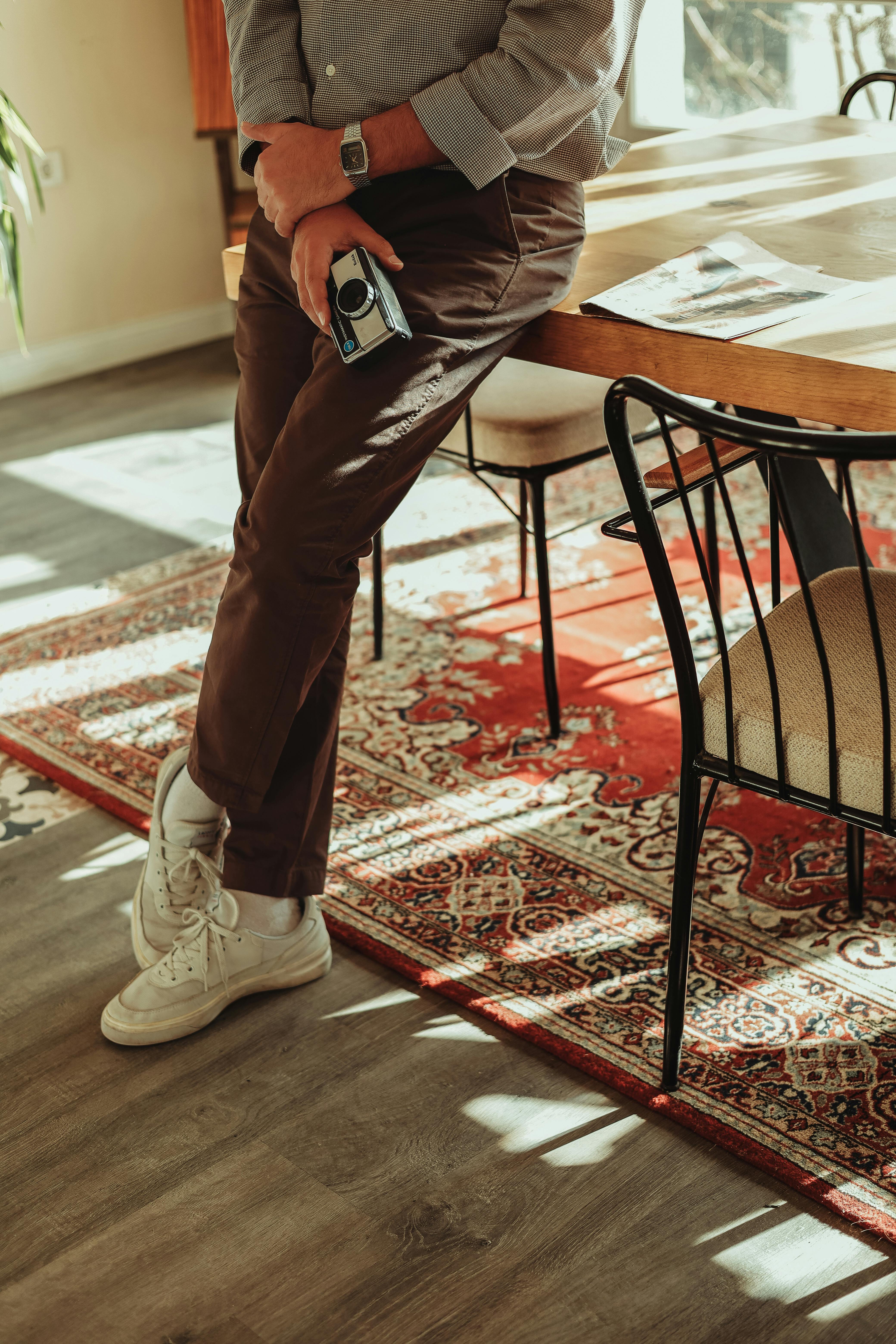 Stylish person leaning on table indoors holding vintage camera in warm sunlight.