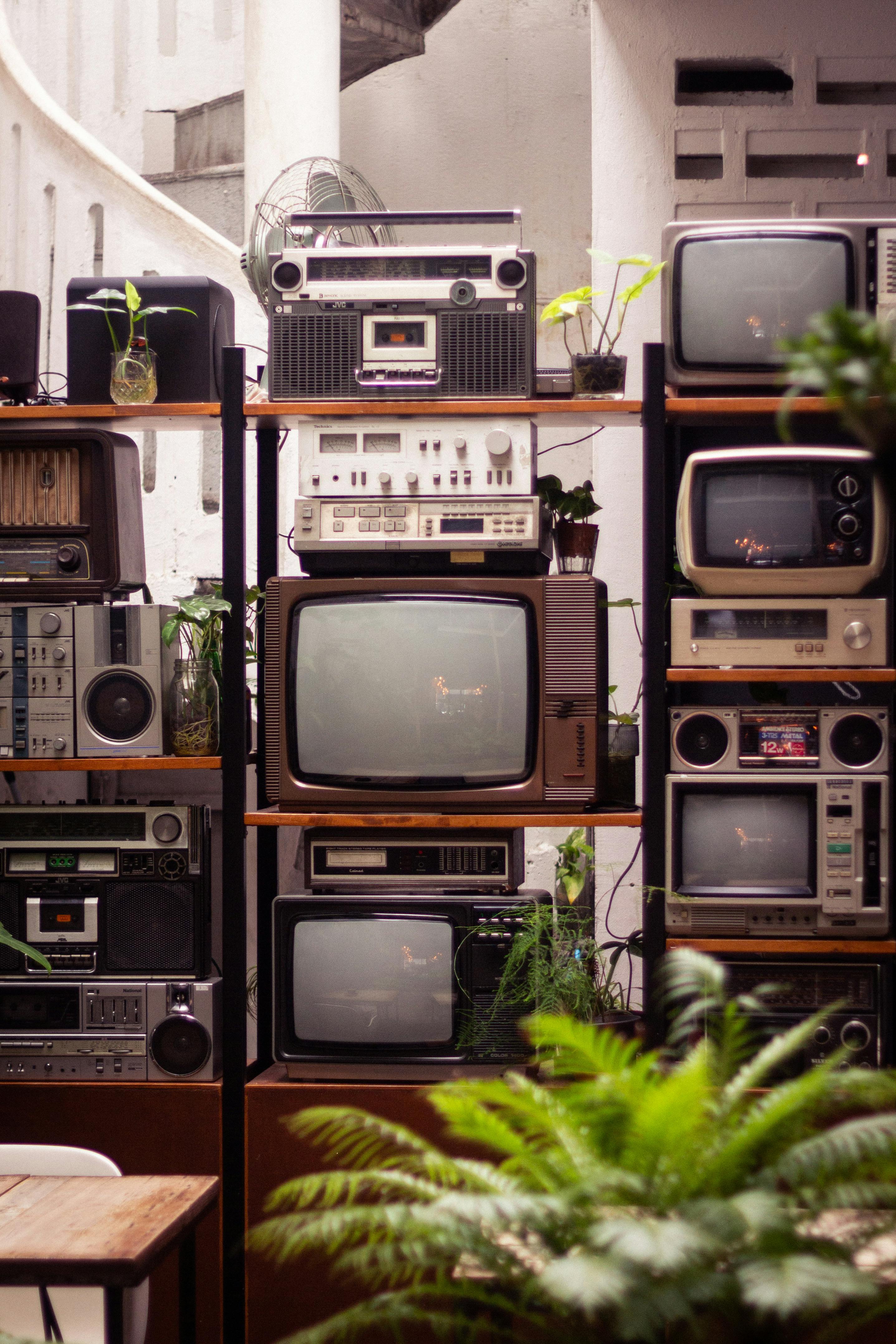 An array of vintage audio and television equipment artfully displayed with lush green plants in Kuala Lumpur.