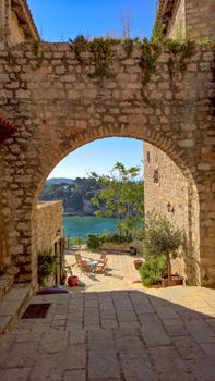 Picturesque view through a stone archway revealing a serene lagoon and rustic courtyard.
