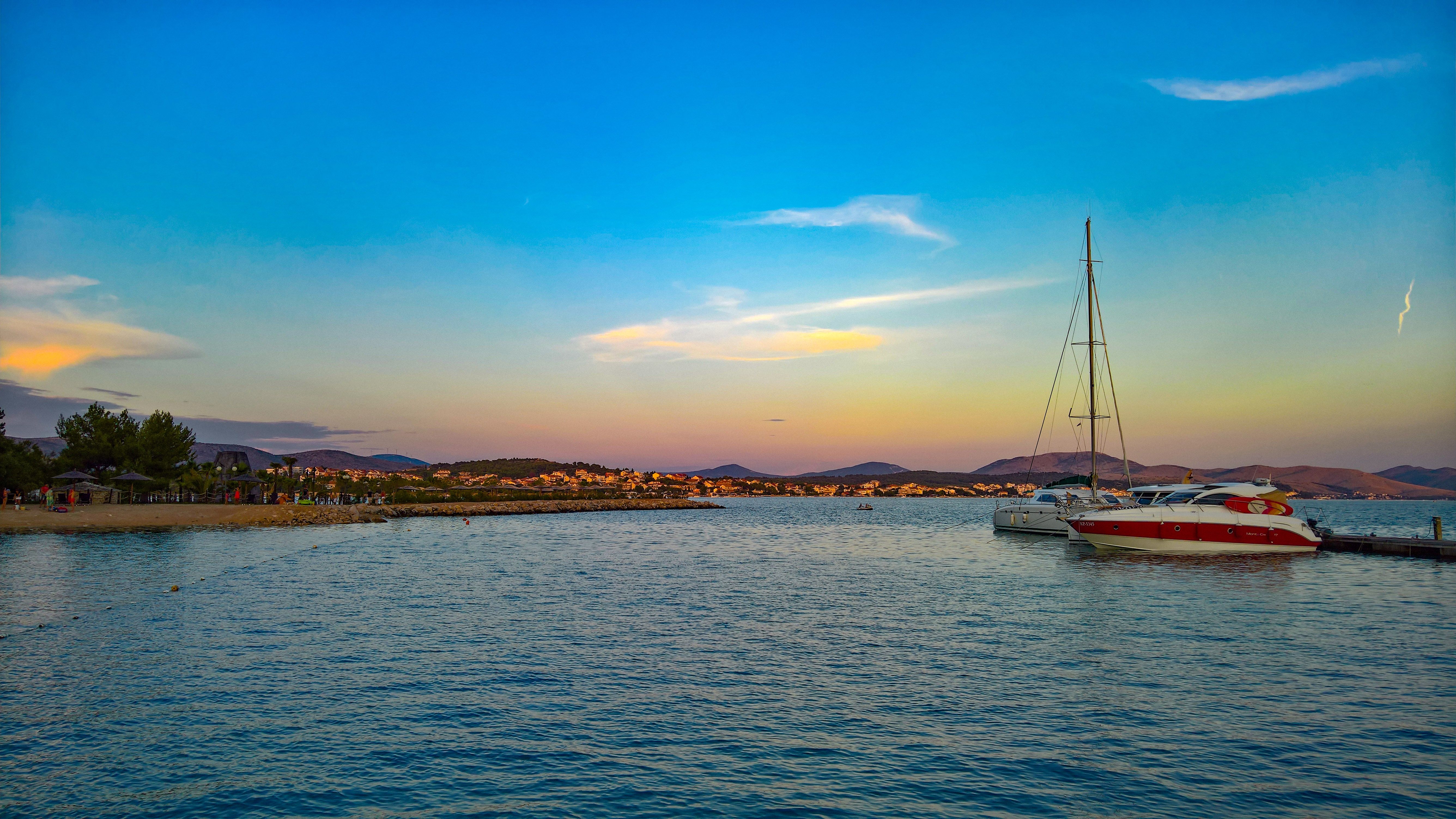 A serene seaside scene at sunset featuring a sailboat docked on calm waters.