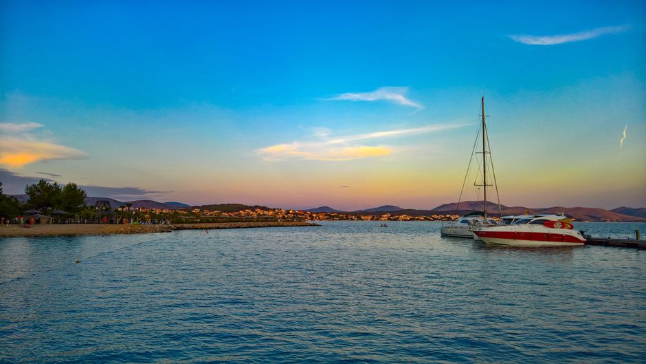 A serene seaside scene at sunset featuring a sailboat docked on calm waters.