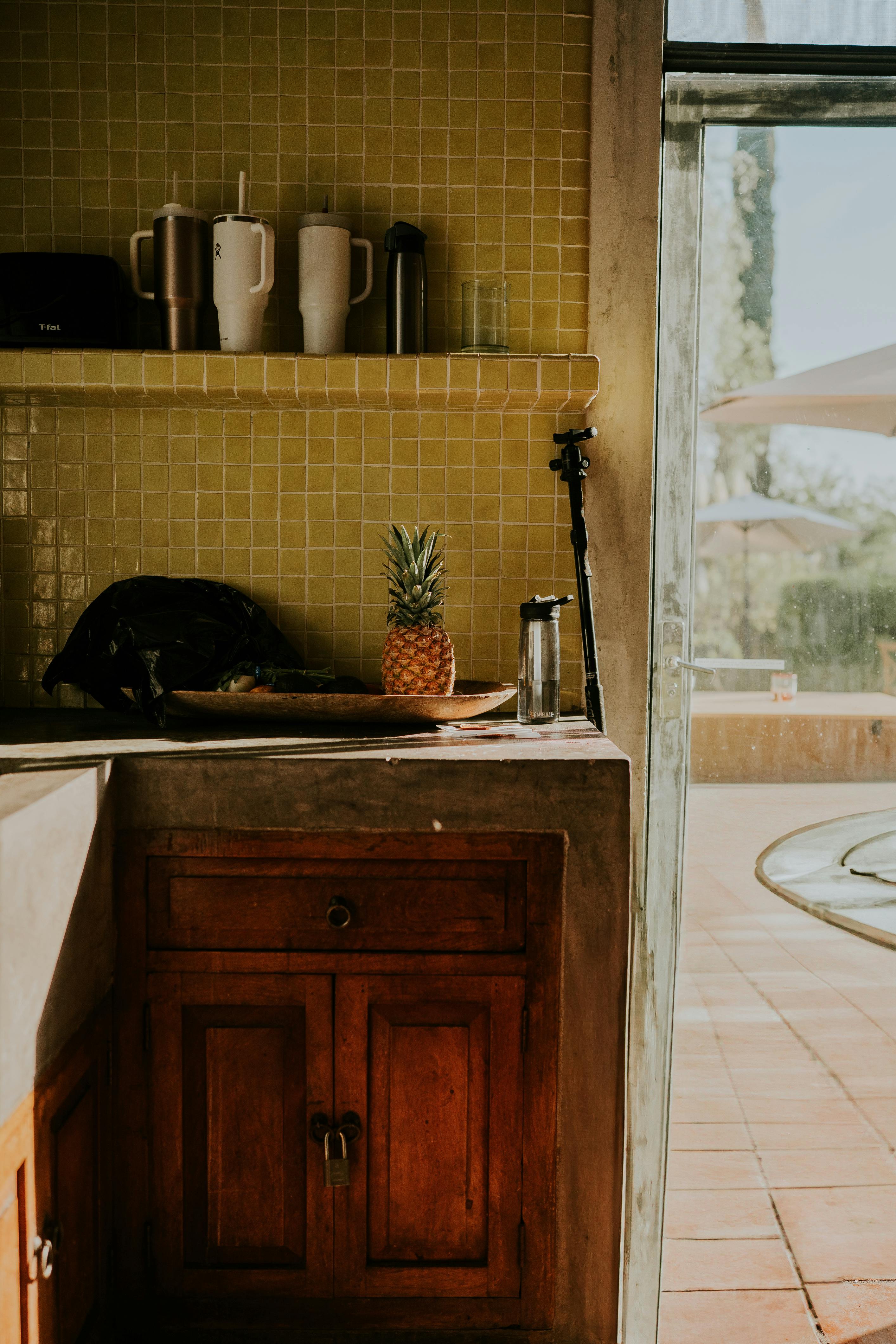 Warm indoor kitchen scene featuring a pineapple and teapots on a tiled counter.