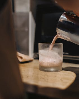A barista expertly pours a cold brew coffee into a glass filled with ice.