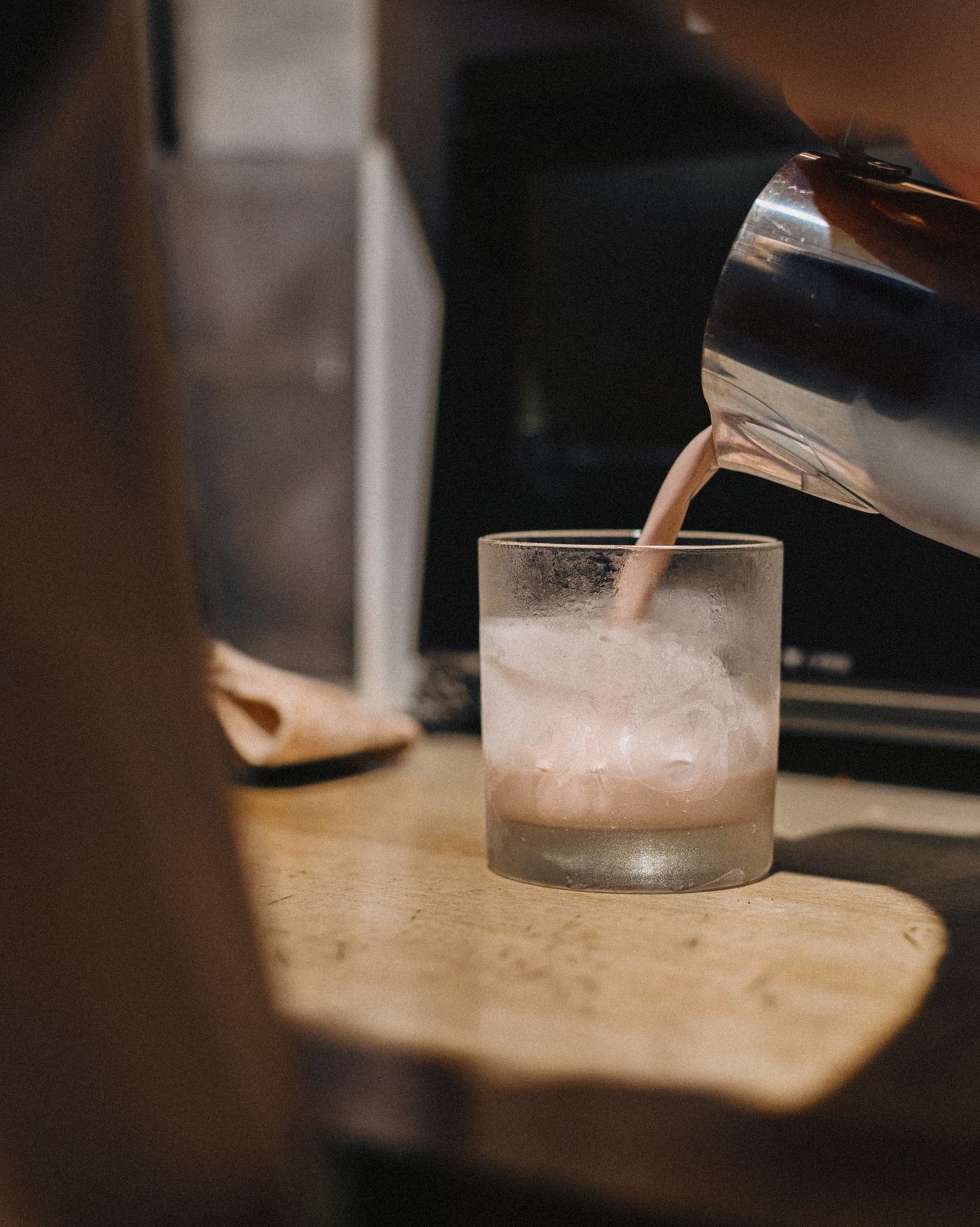 Barista pouring chilled cold brew coffee into a glass filled with ice