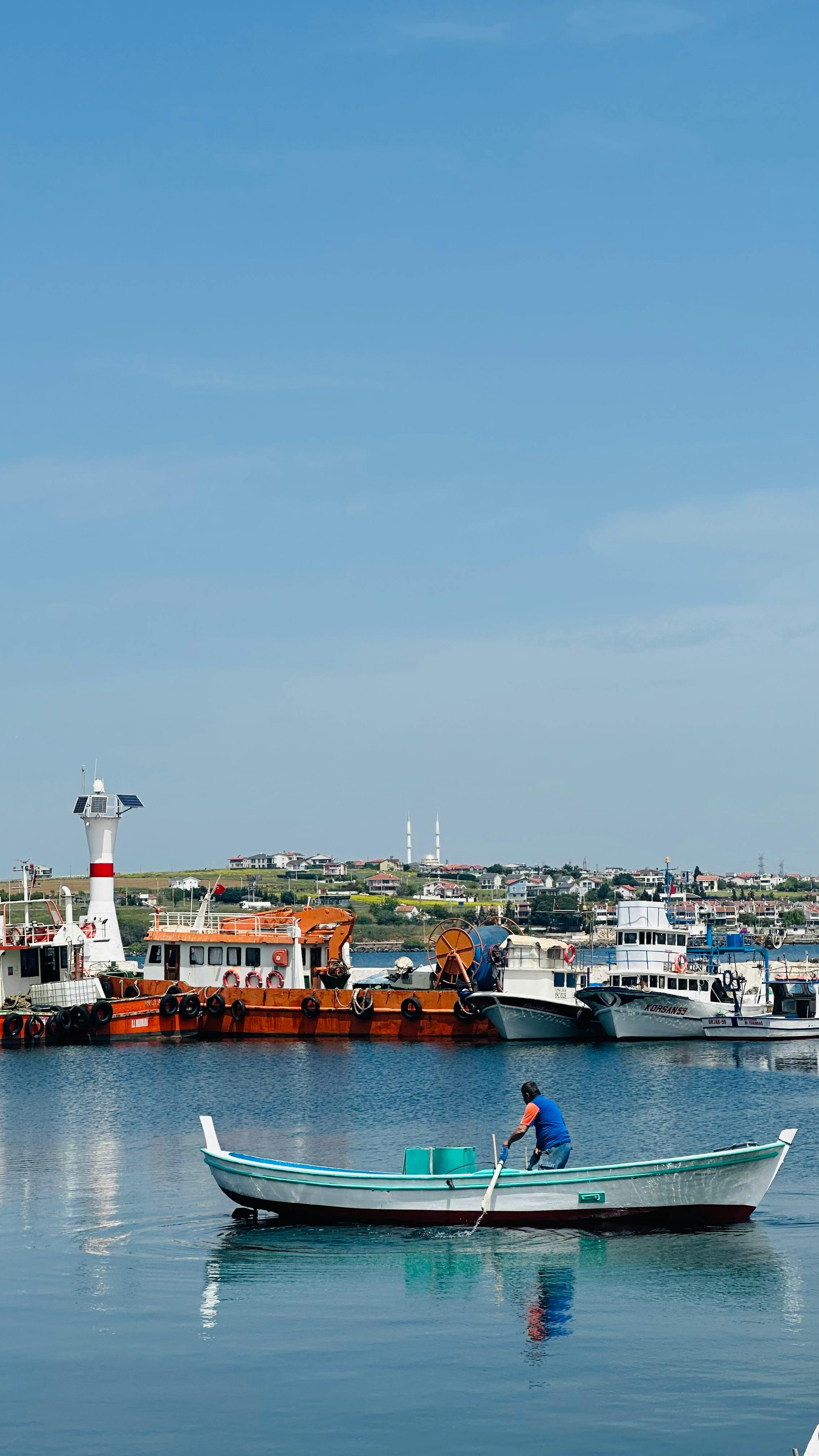 Calm harbor with colorful boats and a lighthouse under blue sky.