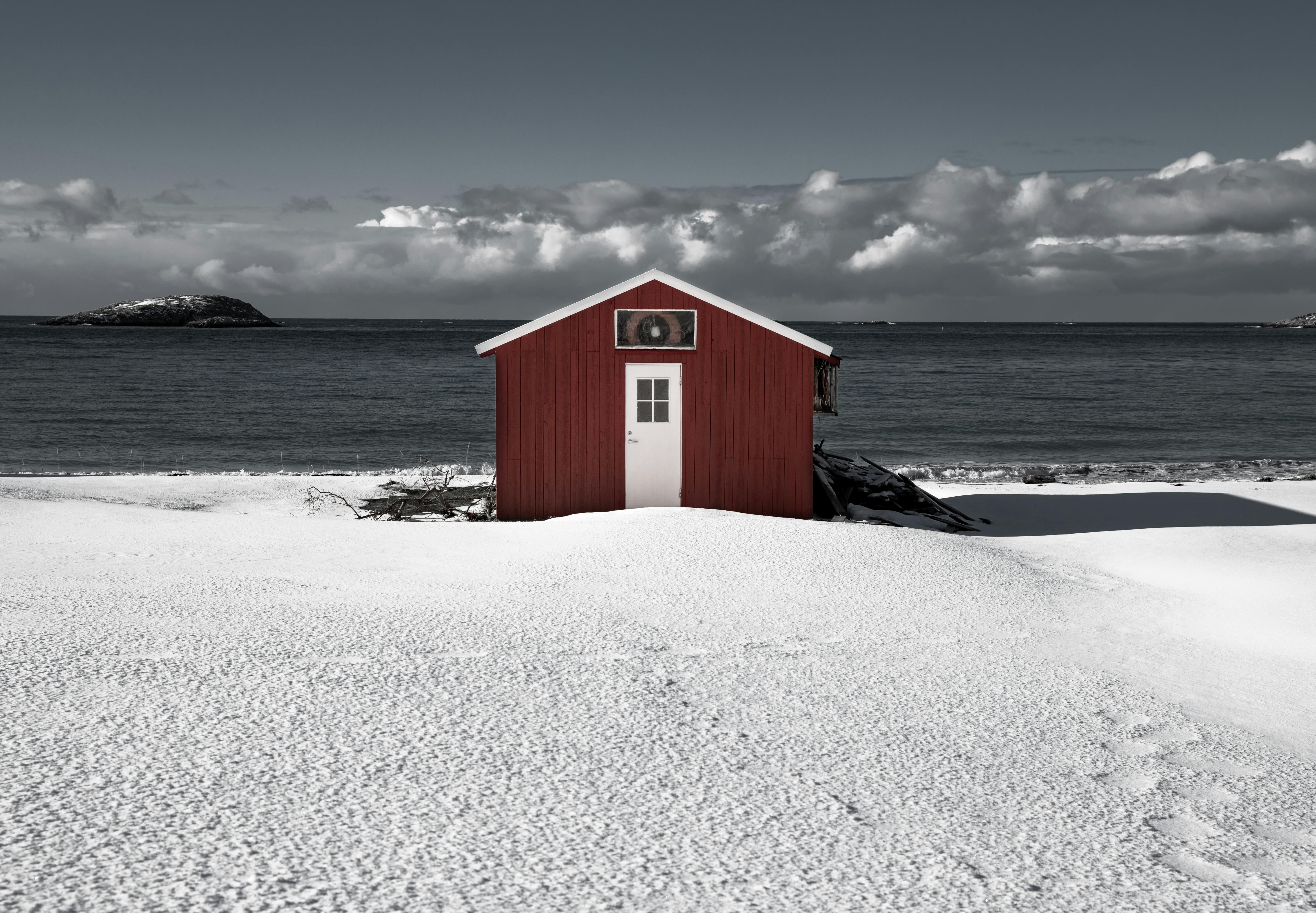 白雪皑皑的海岸线上，一栋红色小屋俯瞰着大海，构成一幅宁静的冬日景象