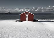 白雪皑皑的海岸线上，一栋红色小屋俯瞰着大海，构成一幅宁静的冬日景象
