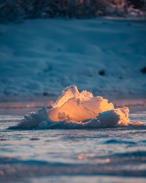 Glowing piece of ice flowing in frozen water in winter time against snowy terrain