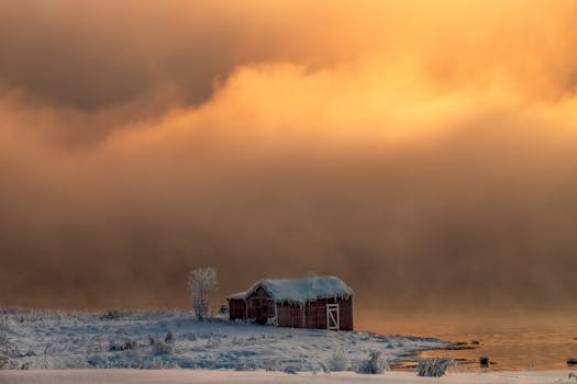 雾蒙蒙的河流和金色的日落天空映衬着风景如画的冬季谷仓
