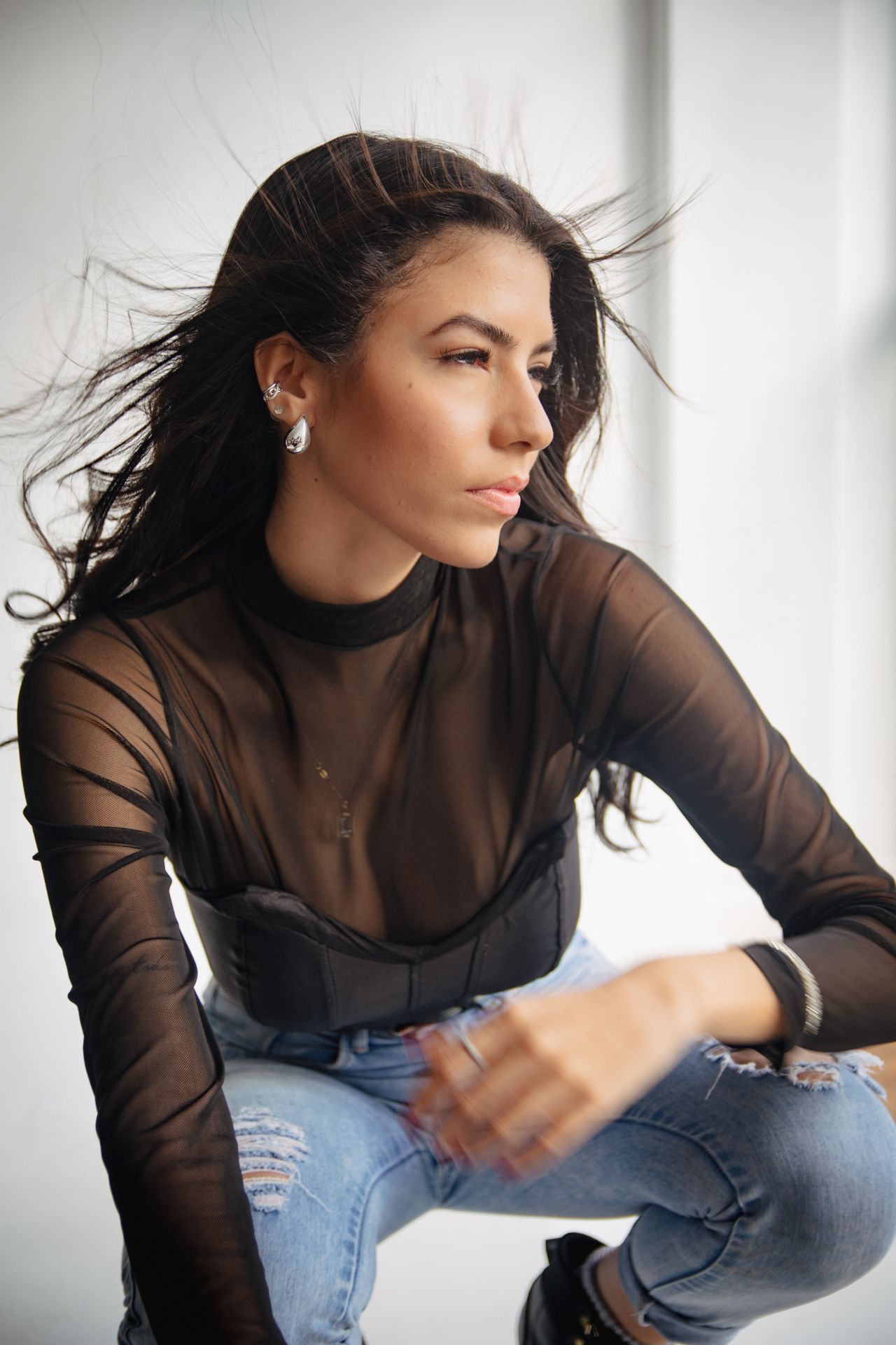 Woman wearing a black sheer mesh long-sleeve top layered over a black bralette with ripped blue jeans