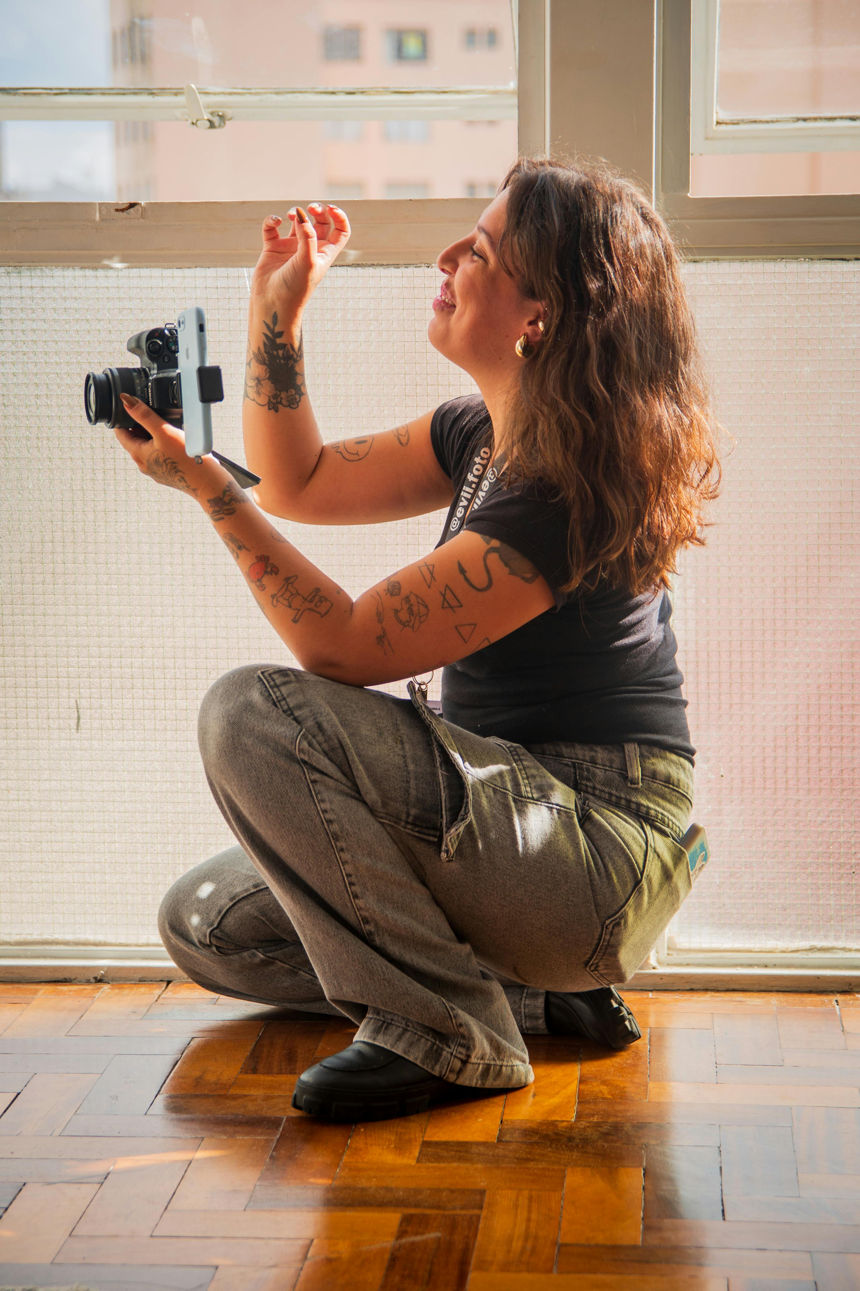 A joyful female photographer with tattoos engaged in an artistic indoor shoot.