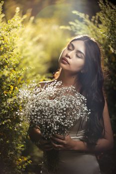 Young woman enjoying a quiet moment with Baby's Breath flowers amidst greenery in warm sunlight.