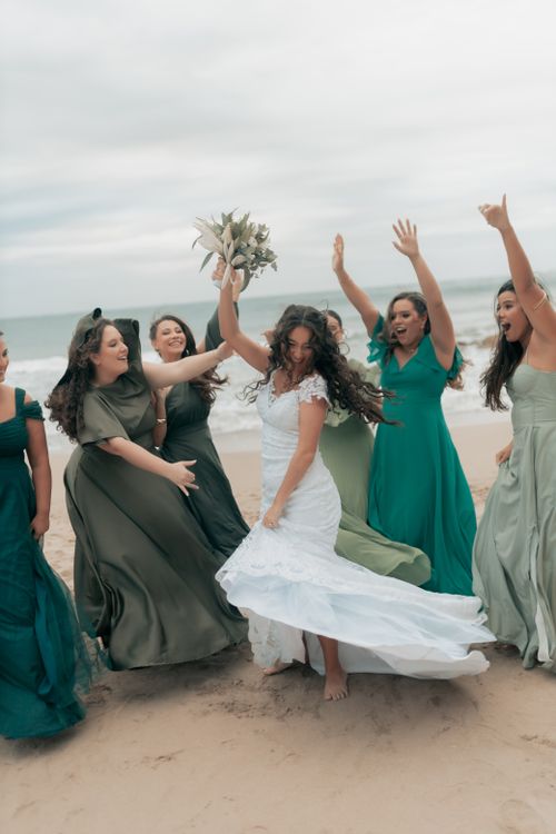 Free Bride and bridesmaids celebrate joyfully on a sandy beach, wearing flowing dresses. Stock Photo