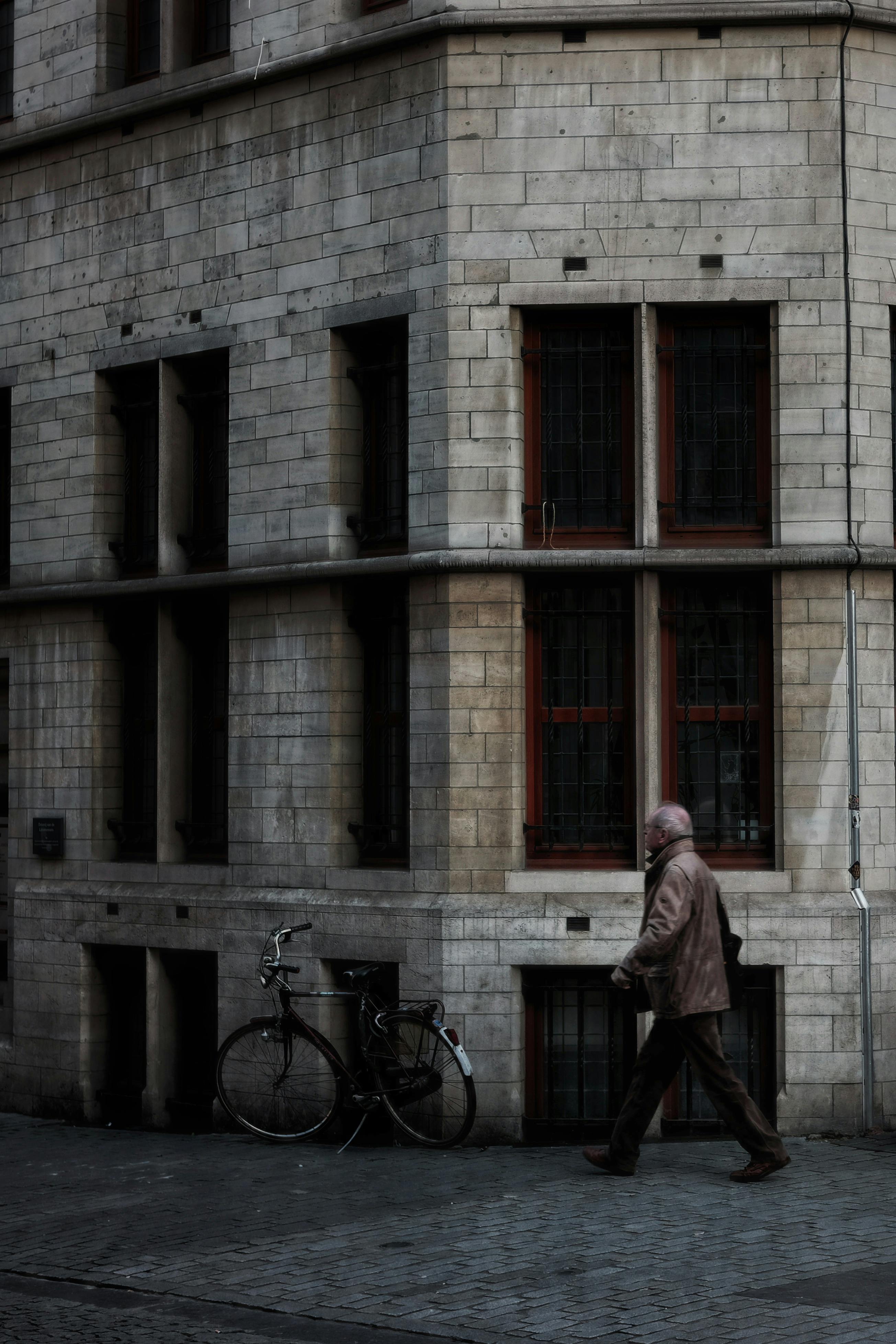 A man walks on a cobblestone street in Leuven, Belgium, near a classic building facade.
