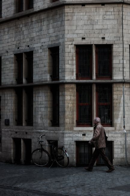 A man walks on a cobblestone street in Leuven, Belgium, near a classic building facade.