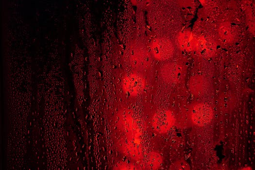 Close-up of raindrops on a red and black surface with bokeh lights creating an abstract, moody effect.