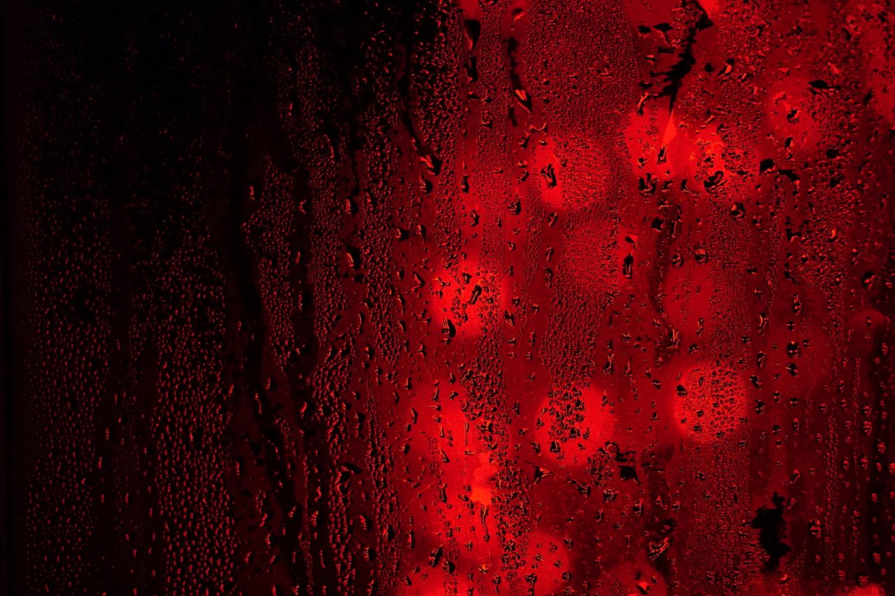close up of raindrops on a red and black surface with bokeh lights cre