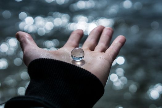 A close-up of a hand holding a glass marble with a beautifully blurred bokeh background.