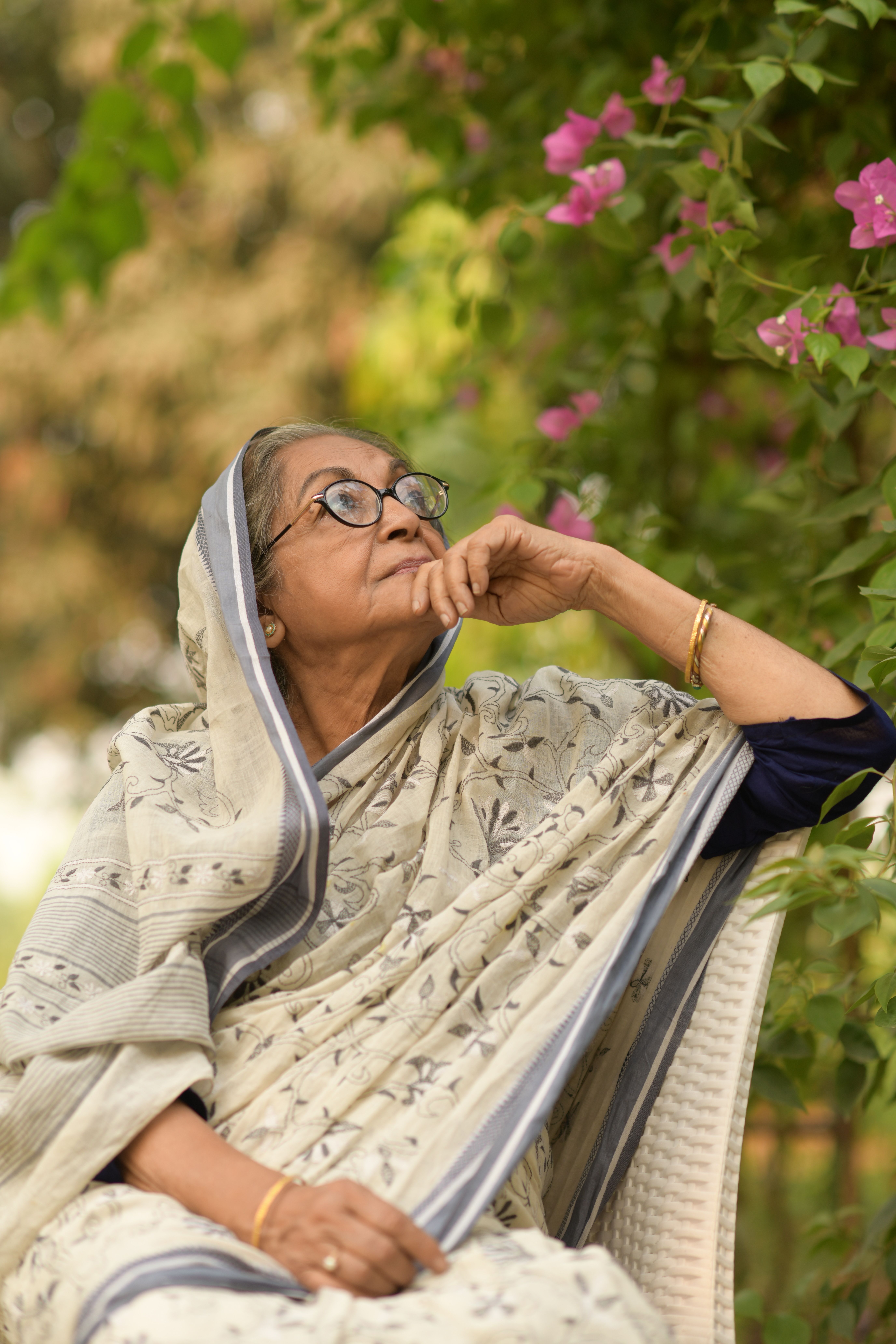 A serene portrait of an elderly woman in traditional attire surrounded by lush garden flowers.