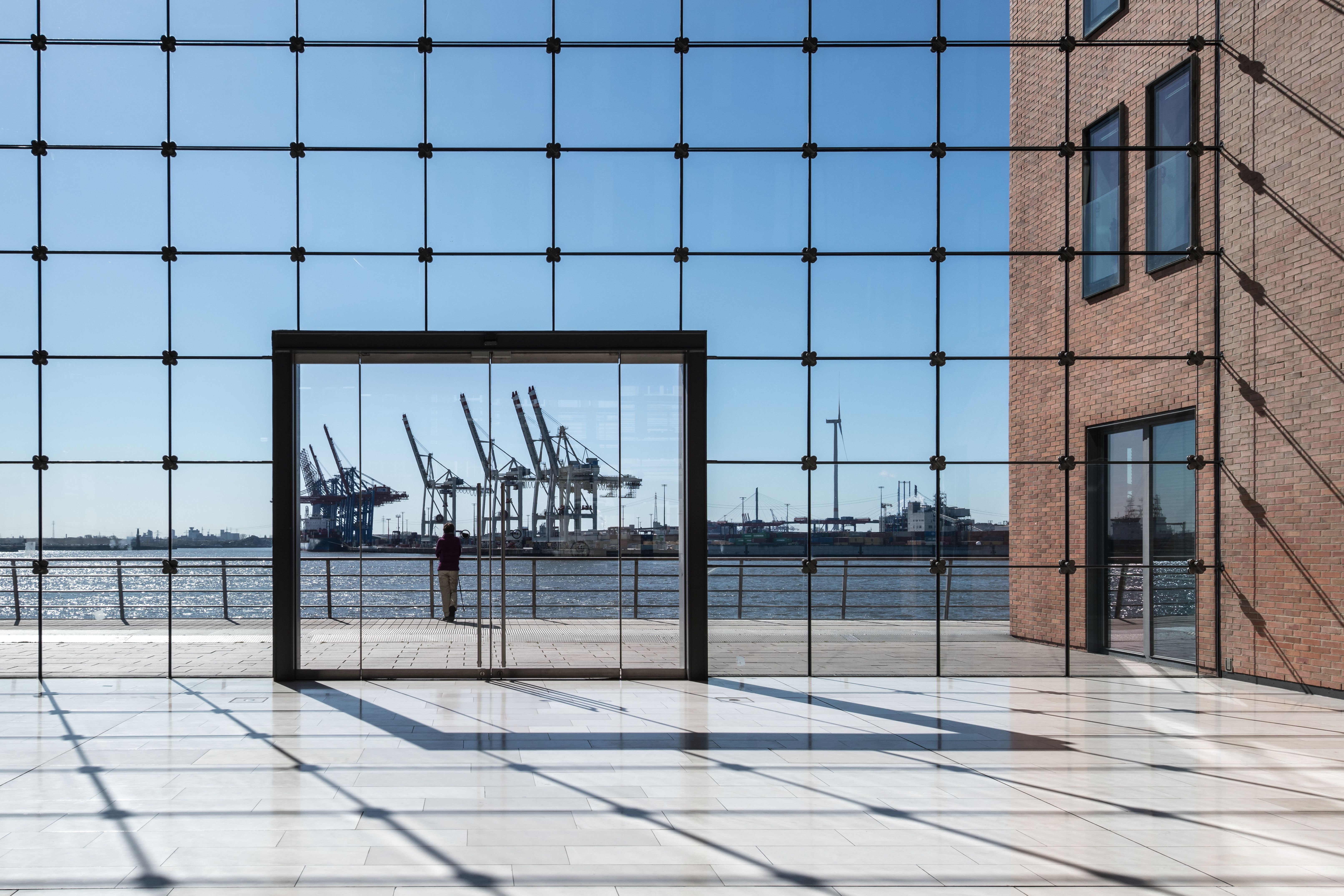 A minimalist architectural rendering of a modern glass-walled office overlooking a serene global harbor with luxury yachts.