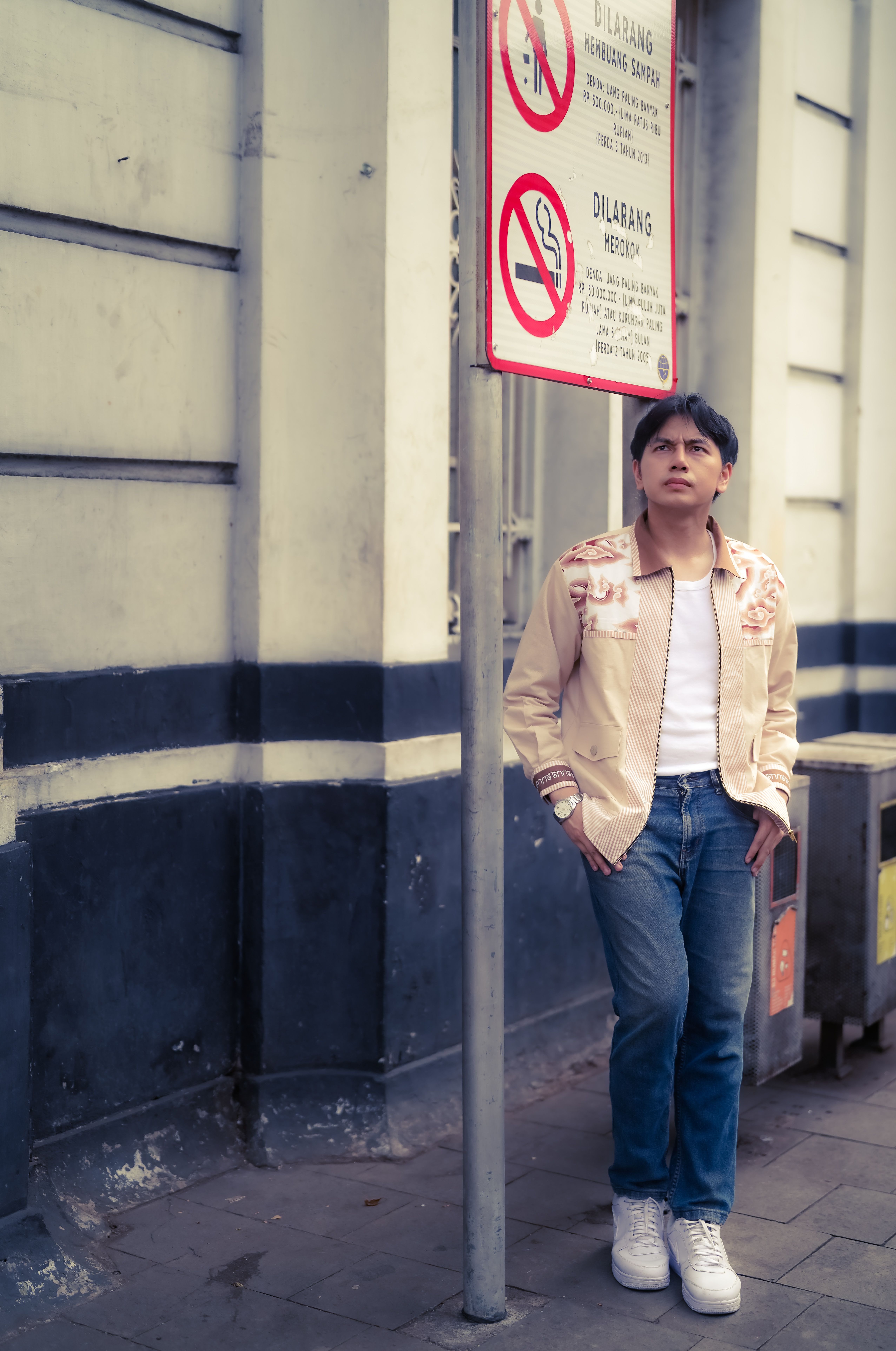 Young man in jeans and jacket stands by a no-littering sign in Jakarta.