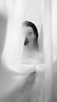 A mysterious and artistic black and white portrait of a woman partially hidden behind sheer white fabric.