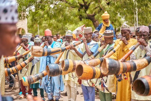 Group of musicians playing large traditional horns during a vibrant outdoor cultural event.