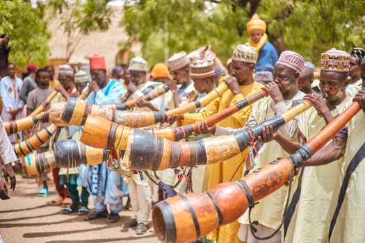 A vibrant display of traditional musicians playing long wooden horns outdoors in a cultural setting.