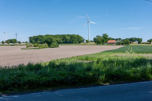 Free A serene rural landscape featuring wind turbines, farmland, and a house under a clear blue sky. Stock Photo