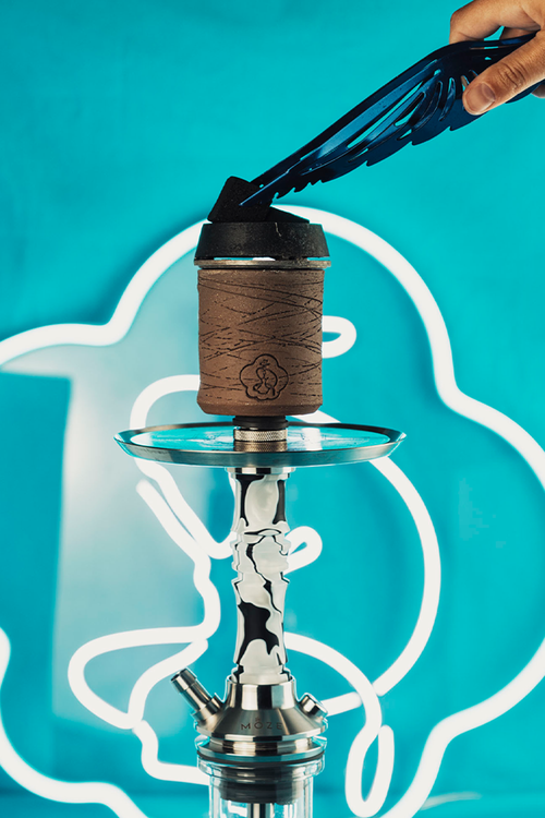 Free Stylish hookah with tongs placing coal, set against a bright neon backdrop, perfect for lifestyle and nightlife themes. Stock Photo