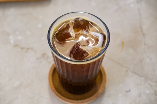 Free A refreshing glass of iced coffee with ice cubes on a wooden coaster, perfect for a summer day. Stock Photo