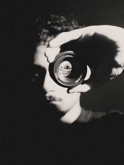 Free Black and white close-up of a person looking through a camera lens, creating a mysterious feel. Stock Photo