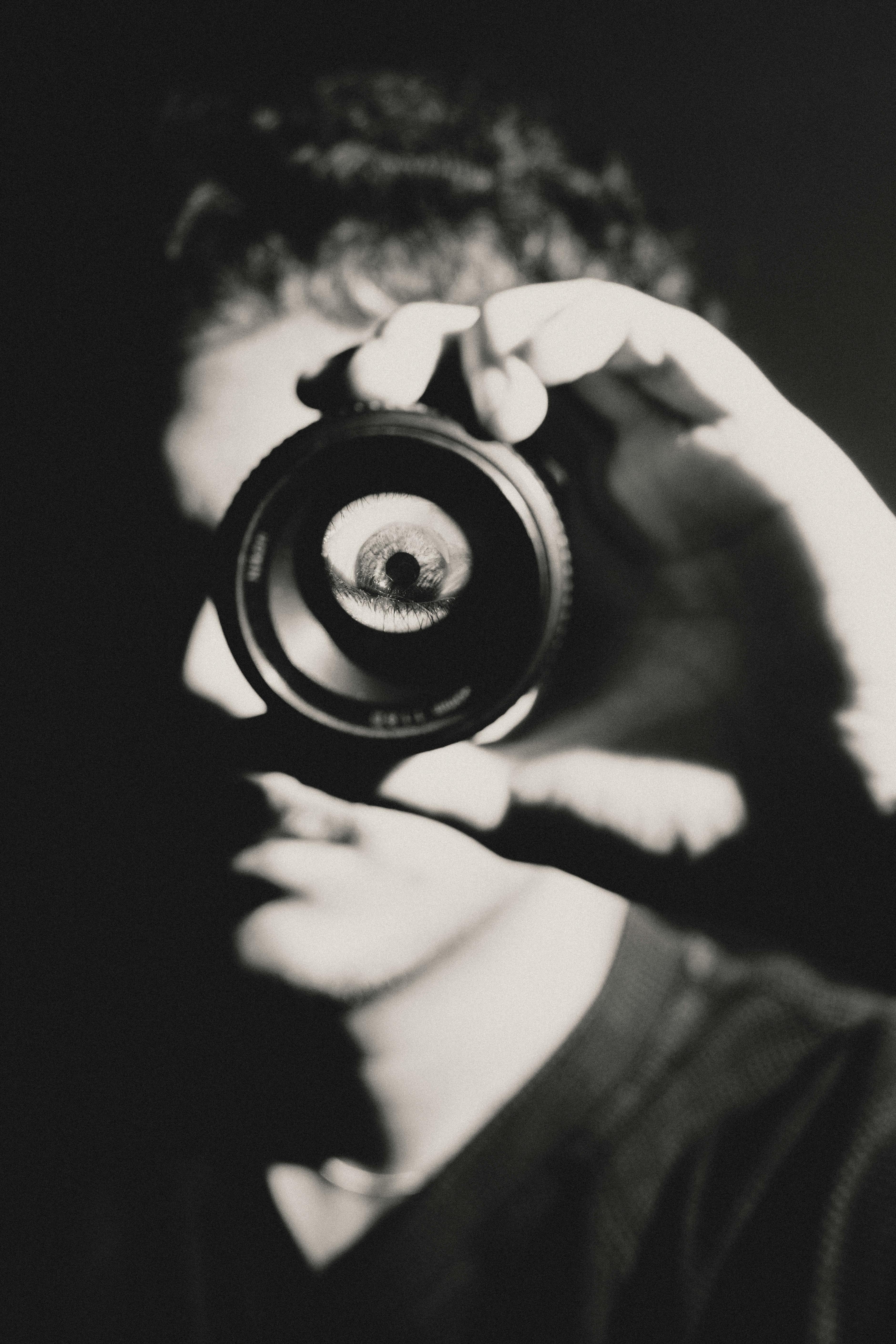 Black and white photo of a person looking through a camera lens, creating an eye illusion.