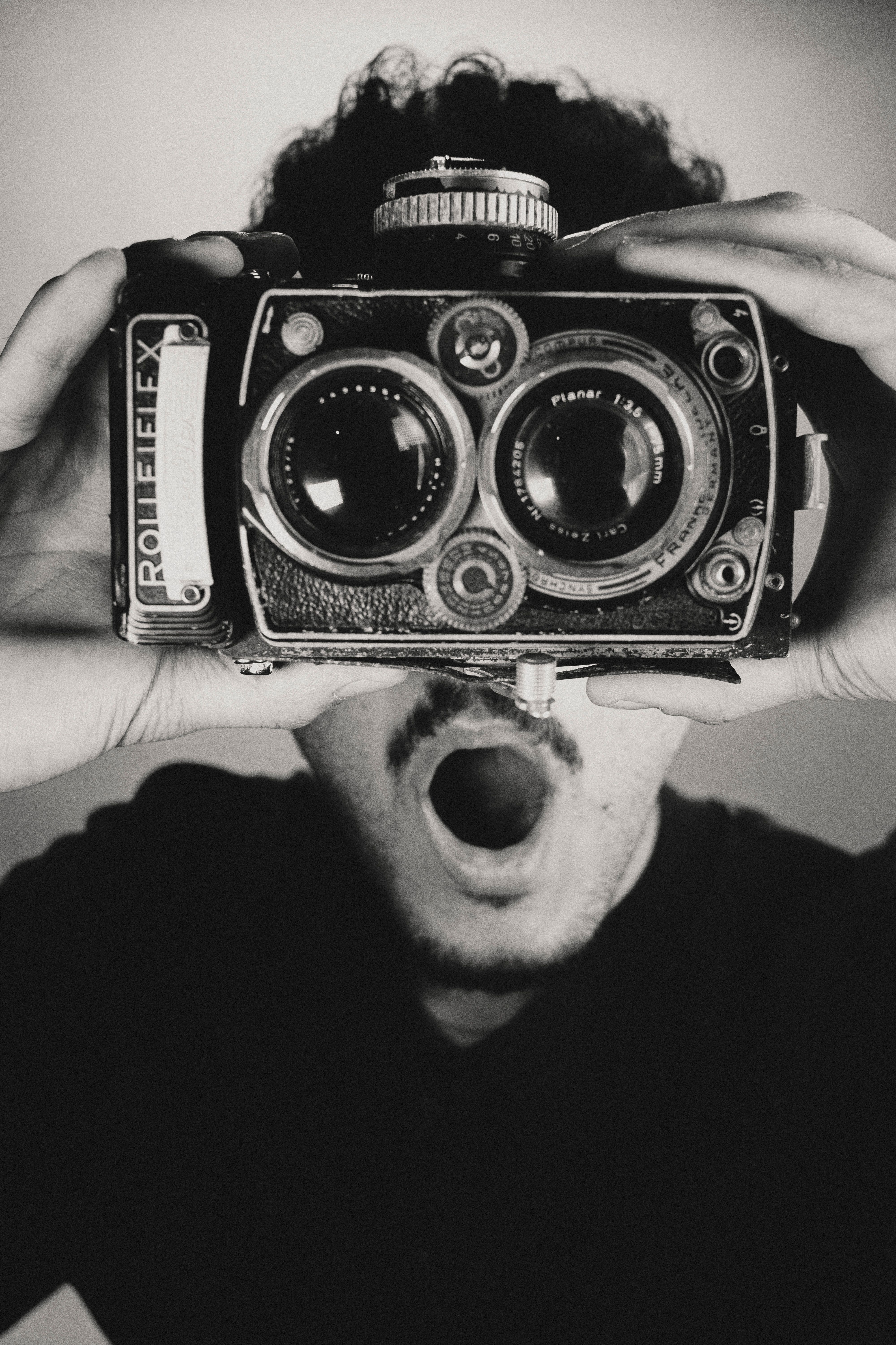 Man holding a vintage Rolleiflex camera, expressing surprise.