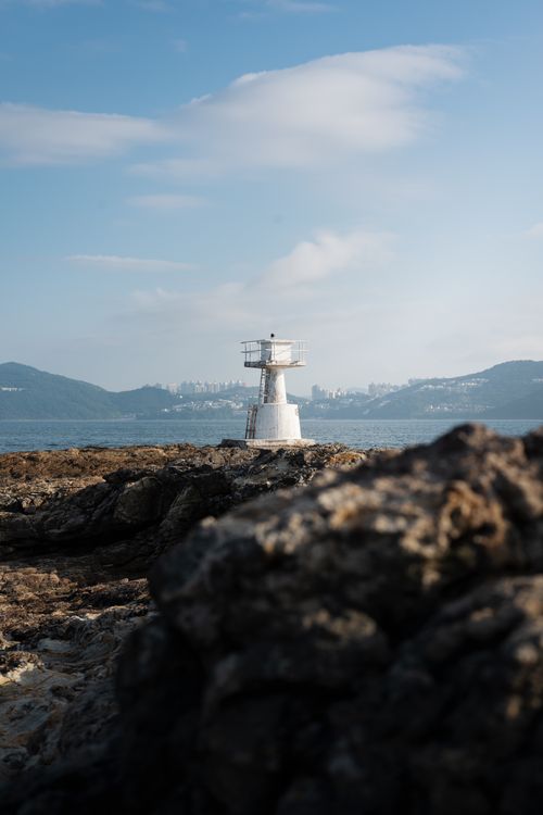 Free Lighthouse overlooking the sea with rocky coast and city skyline in the background. Stock Photo