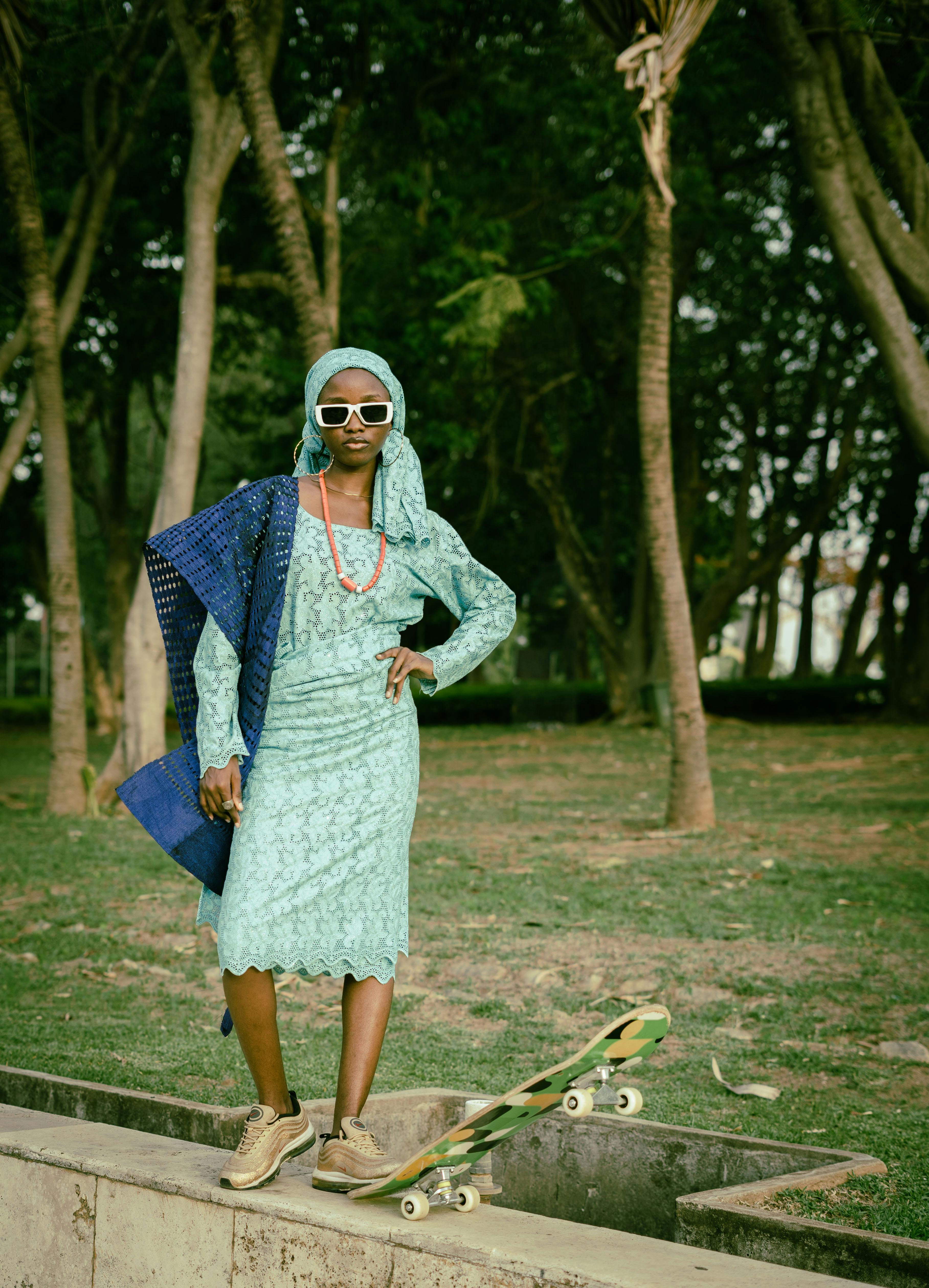 Stylish Nigerian woman in cultural dress and sunglasses in a park with skateboard.