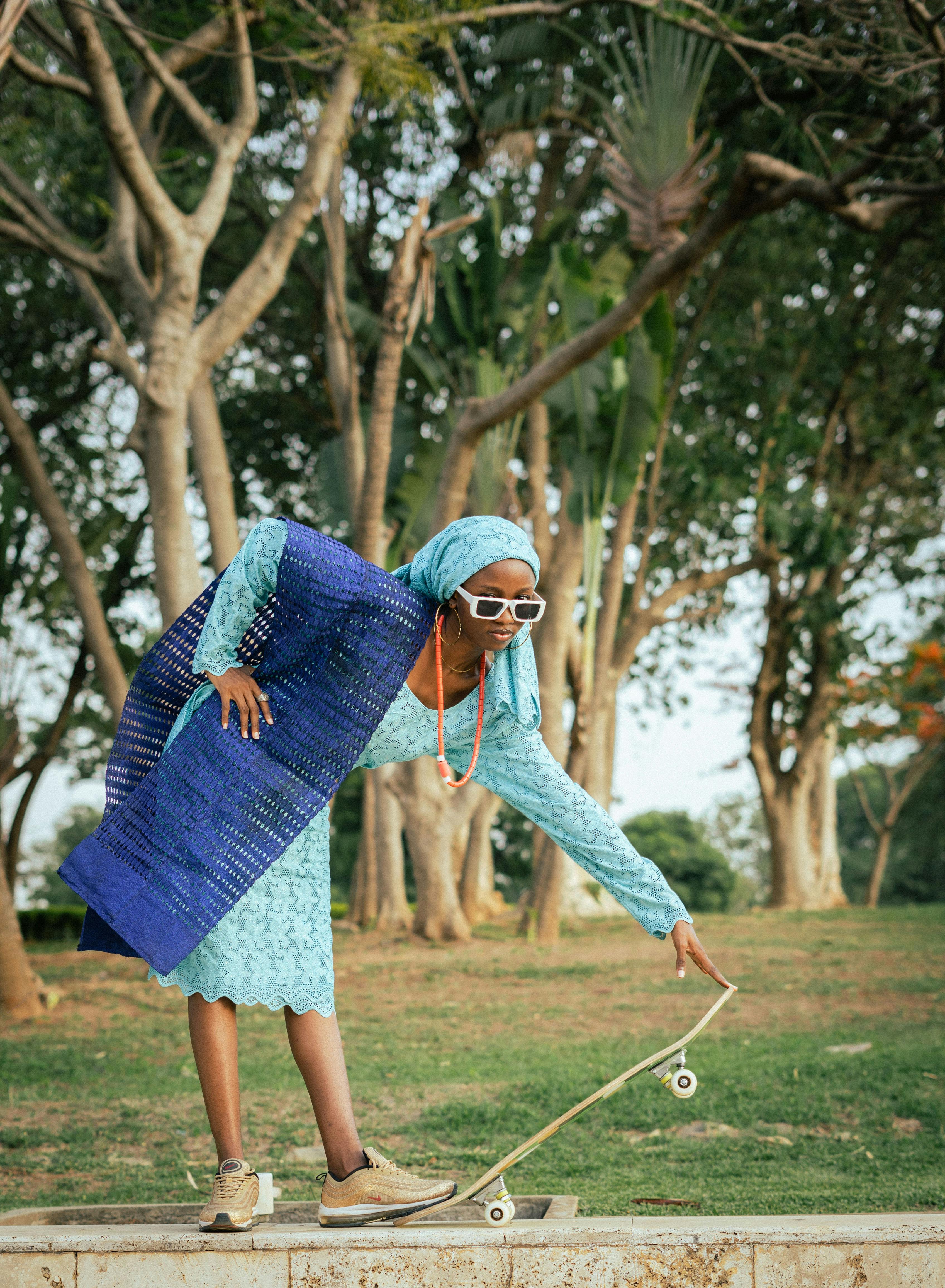 A fashionable woman in traditional dress skateboarding in a Nigerian park.