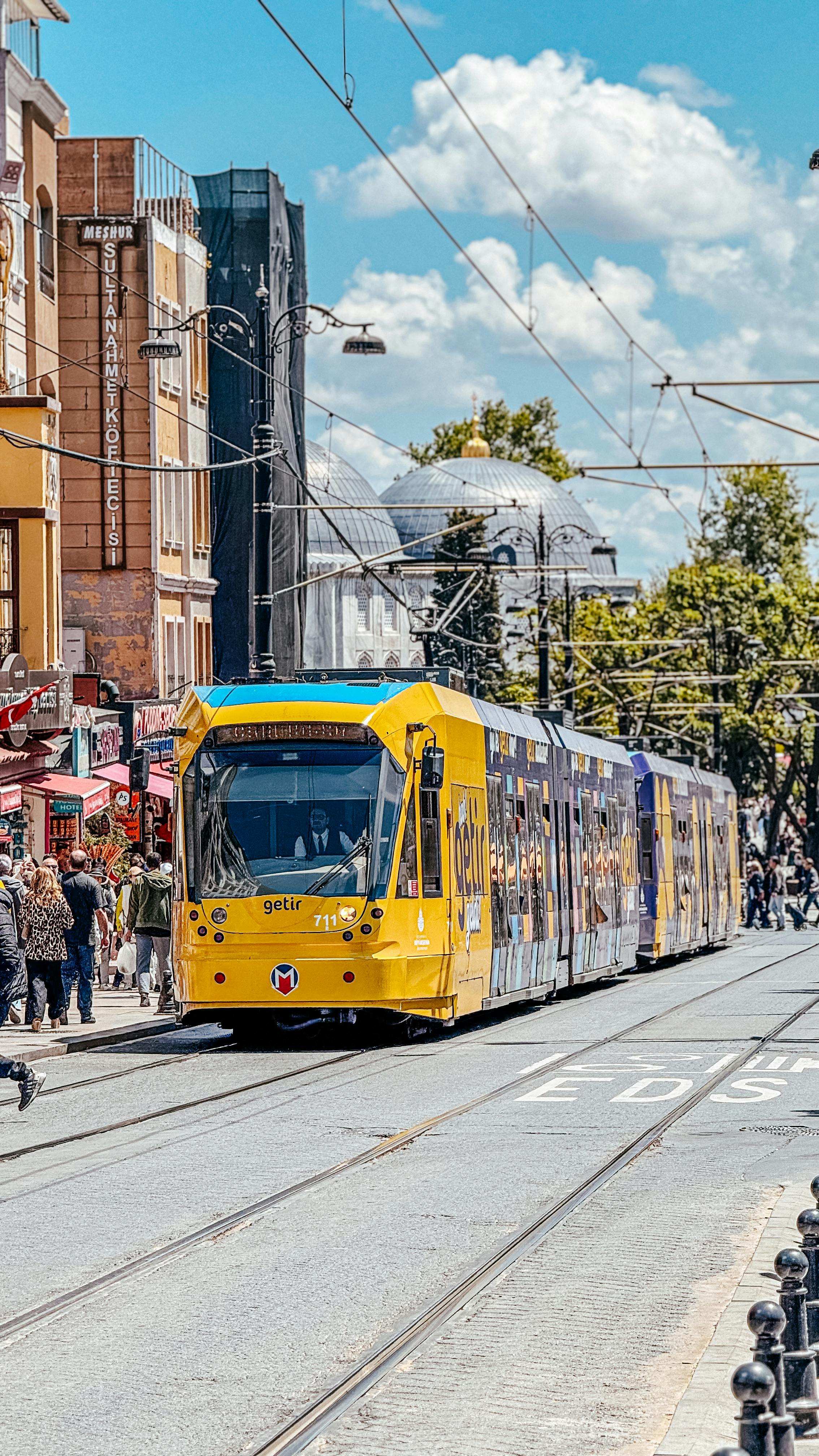 Vibrant yellow tram traveling on a busy street in Istanbul with clear blue skies.