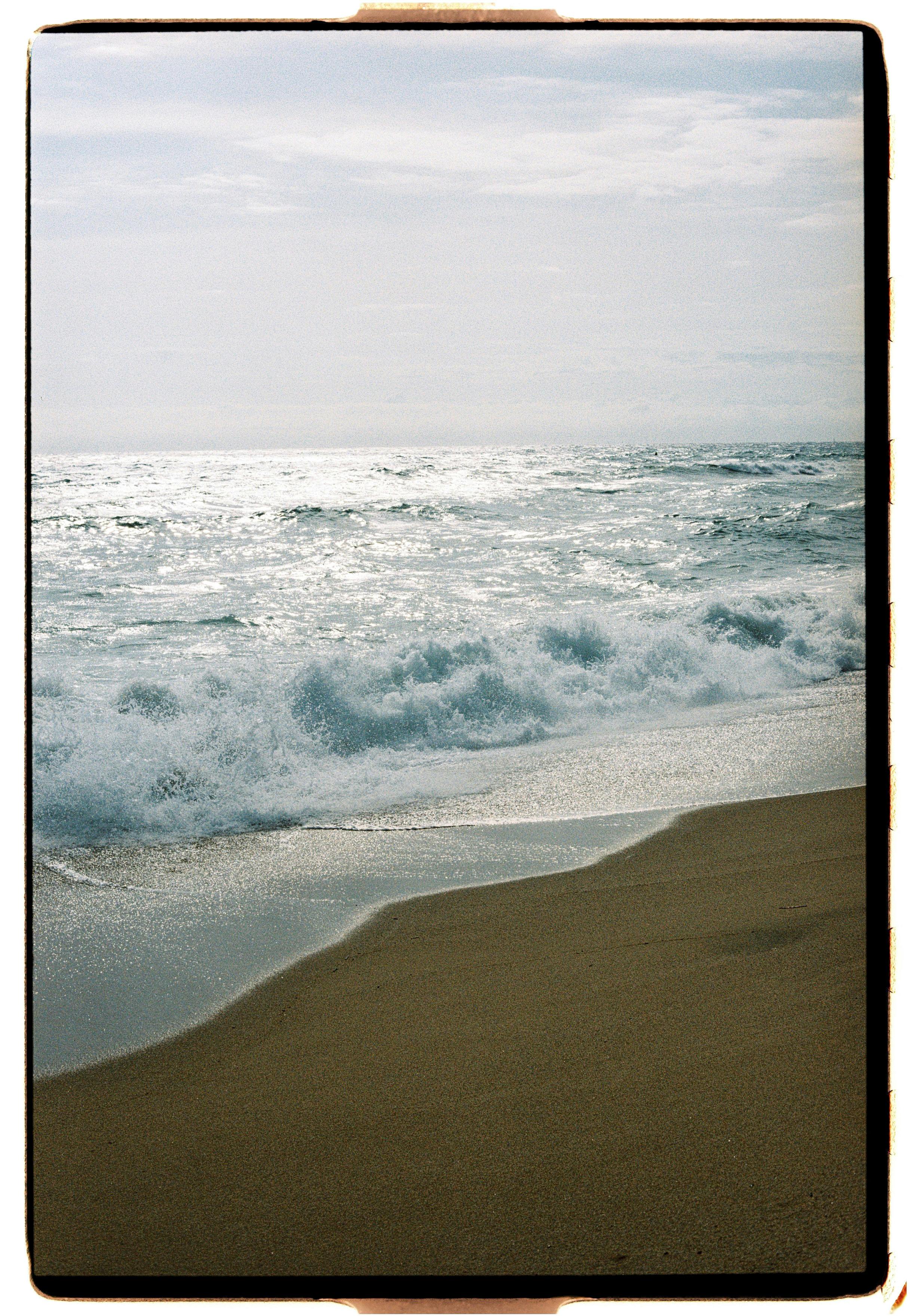 Tranquil seascape capturing ocean waves crashing onto a sandy shore, reflecting sunlight.