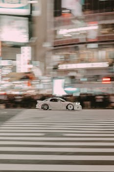 Blurred car racing through bustling Tokyo crosswalk at night, city lights aglow.