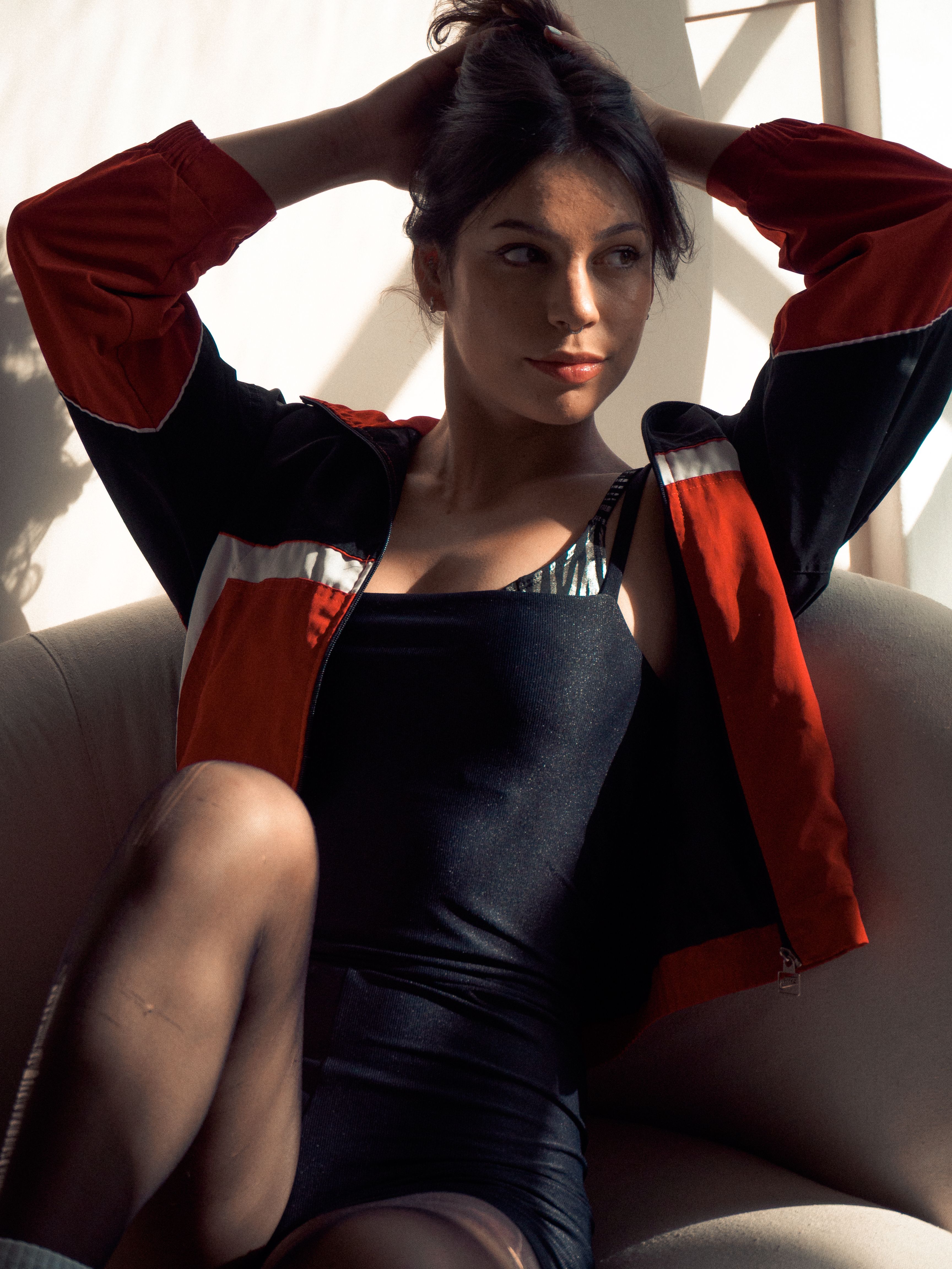 Portrait of a young woman lounging in an armchair wearing casual athletic wear, basking in natural light.
