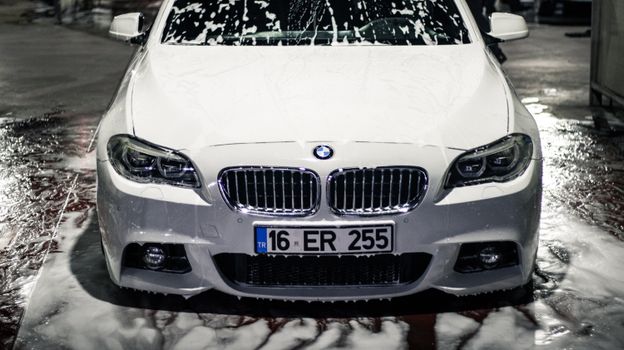 White BMW car under cleaning, covered in soap at a car wash in Bursa, Türkiye.