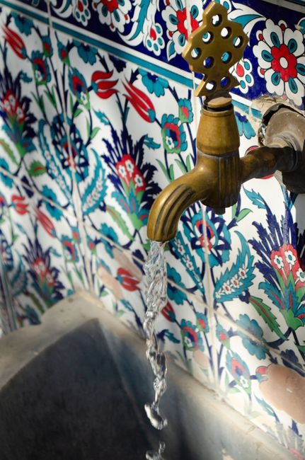 A decorative fountain tap with flowing water set against vibrant, intricately patterned tiles.