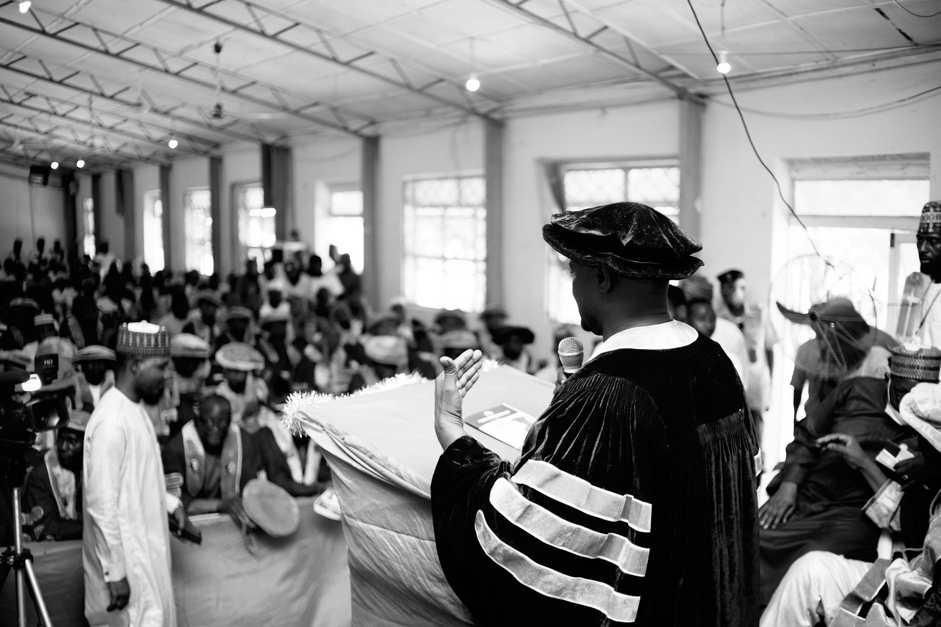 Academic ceremony with a speaker addressing a diverse audience indoors.