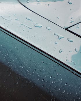 Close-up of raindrops on a sleek metallic car surface, showcasing texture and reflection.