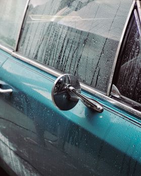 Close-up of a classic car side with raindrops, highlighting vintage design and mood.