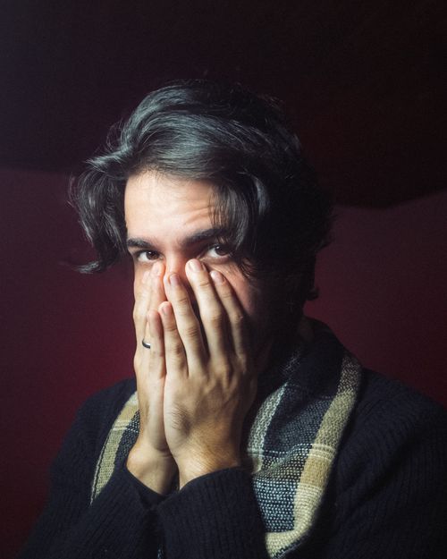 Free Close-up portrait of a young man covering his face thoughtfully. Indoor setting with moody lighting creates an introspective atmosphere. Stock Photo